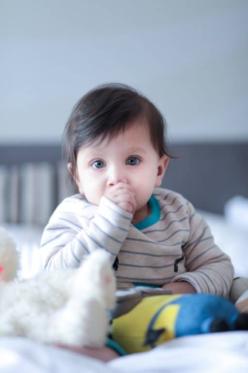 Baby sitting in a crib sucking his thumb