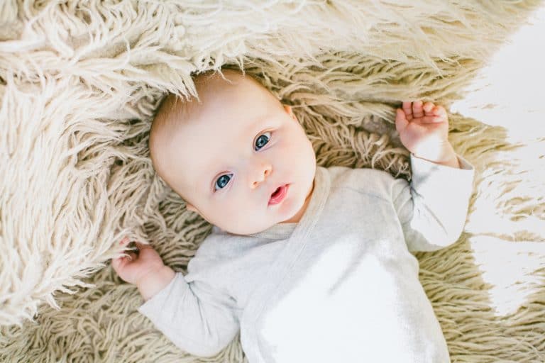 baby in white onesie laying on a fluffy blanket