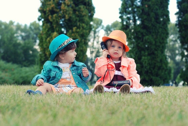 Little kids sitting outside talking on a phone 