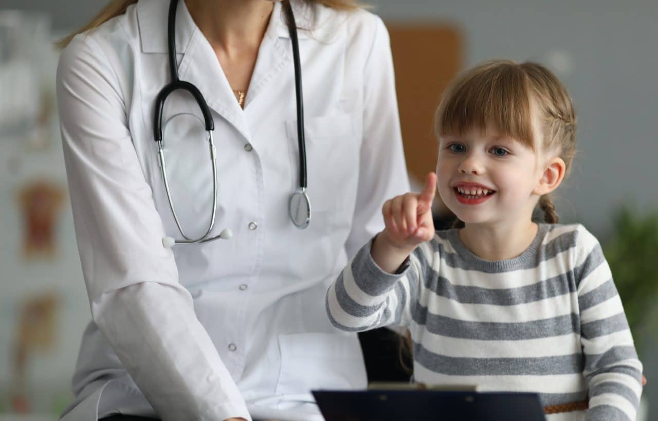 Close-up of smiling child pointing finger and holding paper folder. Happy kid looking at camera with gladness and smiling. Healthcare and prevention concept