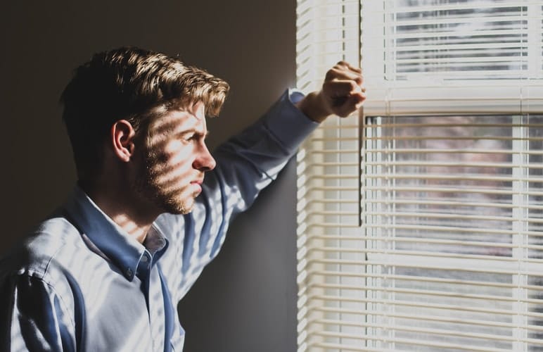 A man stares outside of a window in his home.
