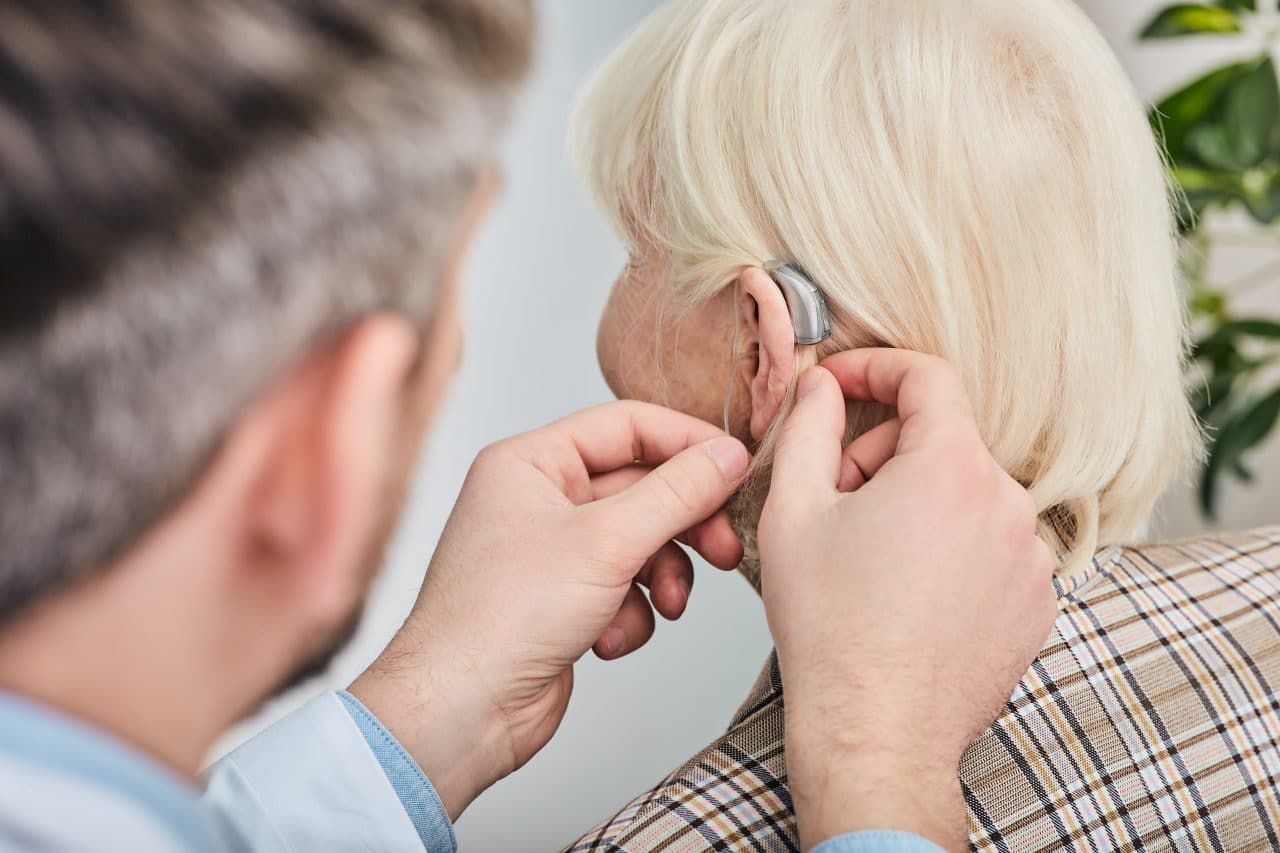 Audiologist fitting a hearing aid on an older female patient.