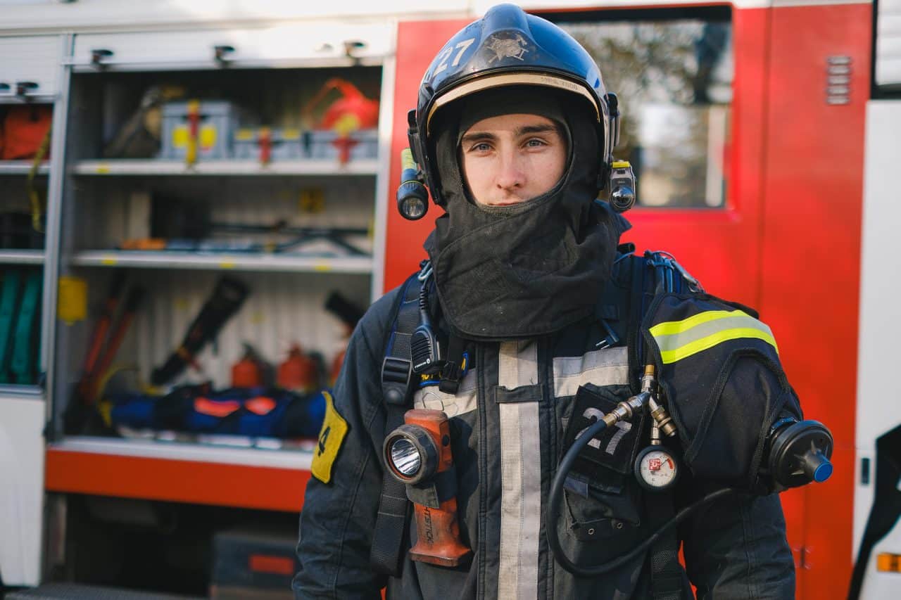 Firefighter in uniform standing in front of a firetruck.