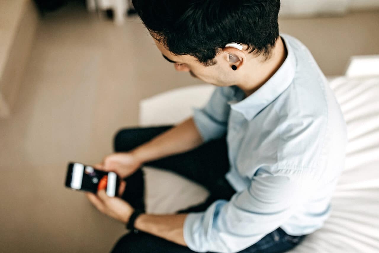Young man with a hearing aid looking at his smartphone.