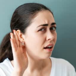 Woman with her hand up to her ear straining to hear