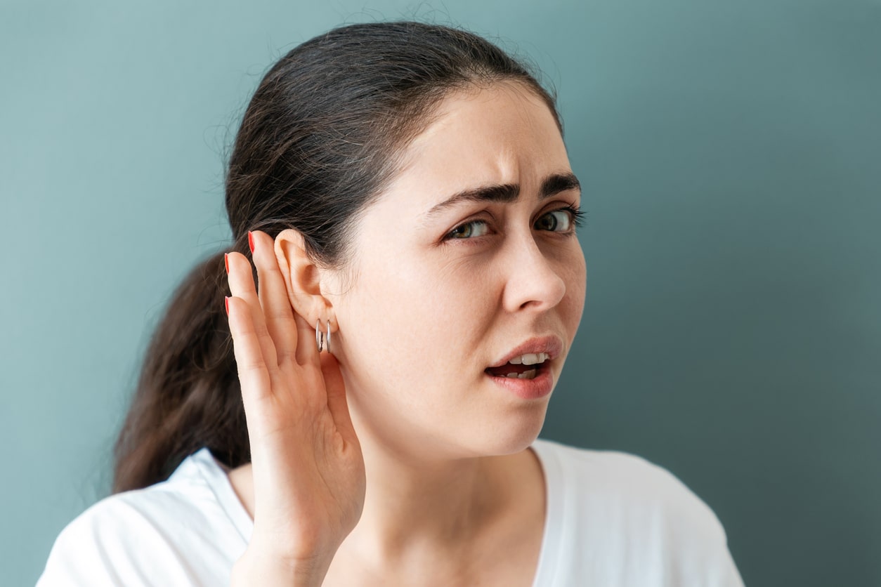 Woman with her hand up to her ear straining to hear.
