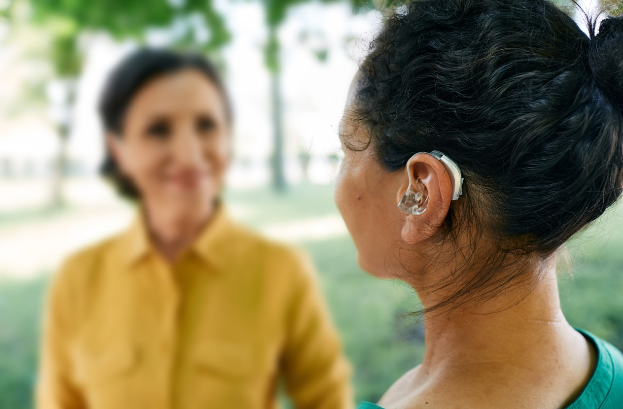 Woman with a hearing aid talking to a friend in a park.