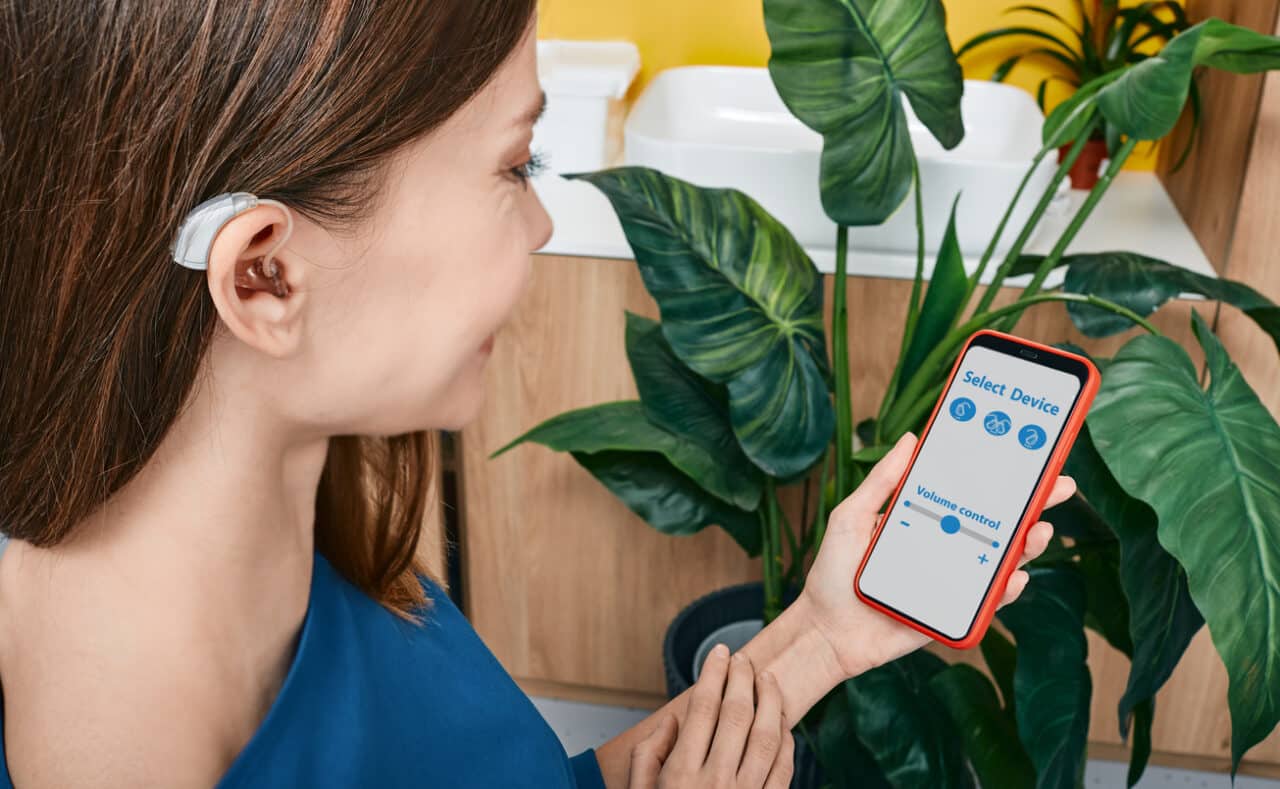 Person wearing a hearing aid uses her hearing aid smartphone app to adjust the volume settings.